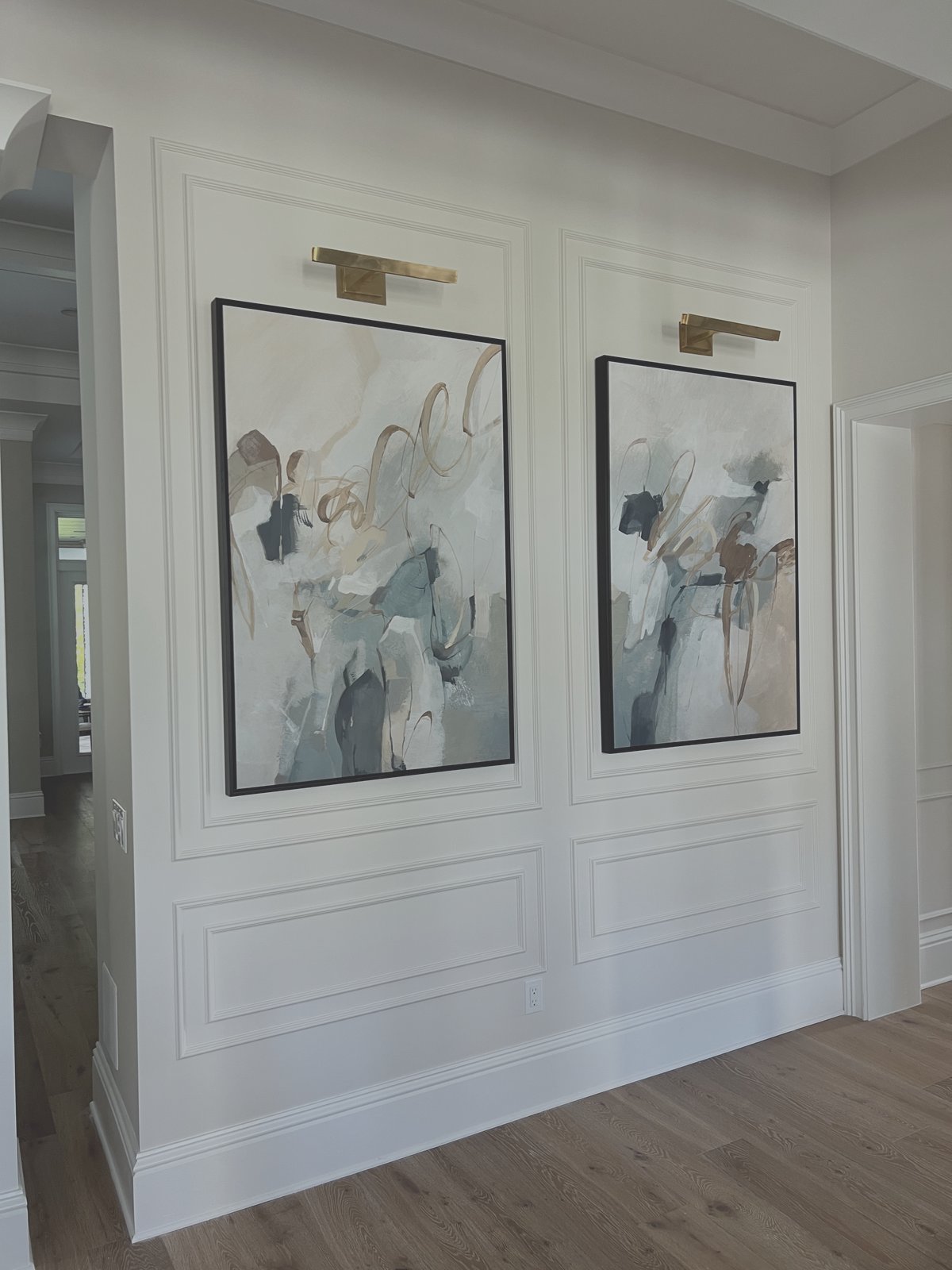 Dual picture frame wainscoting wall panels with brass art sconces and custom baseboard trim